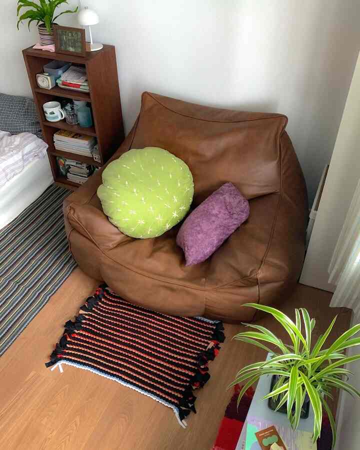 ブラウンの木目調とグリーンの植物が調和した小さな寝室、ブラウンのビーズクッションとラグが配置された温かみのある空間