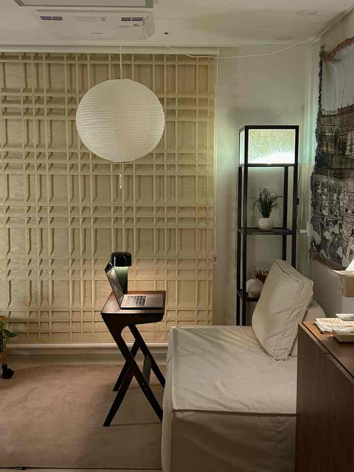 ベージュと木目調のワンルームリビング、サイドテーブルと照明、ブラインドが配置された雰囲気のあるインテリア