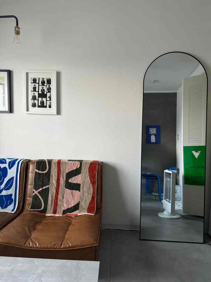 Modern living room with white walls and brown leather sofa featuring a large full-length mirror creating a sense of spaciousness