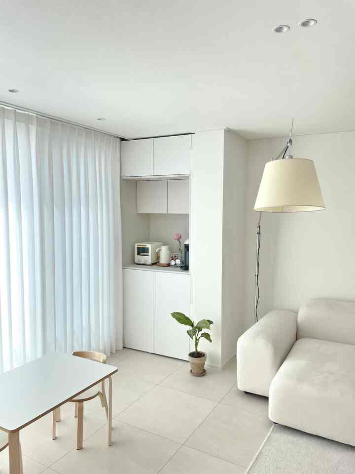 白を基調としたリビング空間、耐力壁の後ろに設置された収納兼ホームバーと小型家電が配置された、清潔感のあるミニマルなインテリア