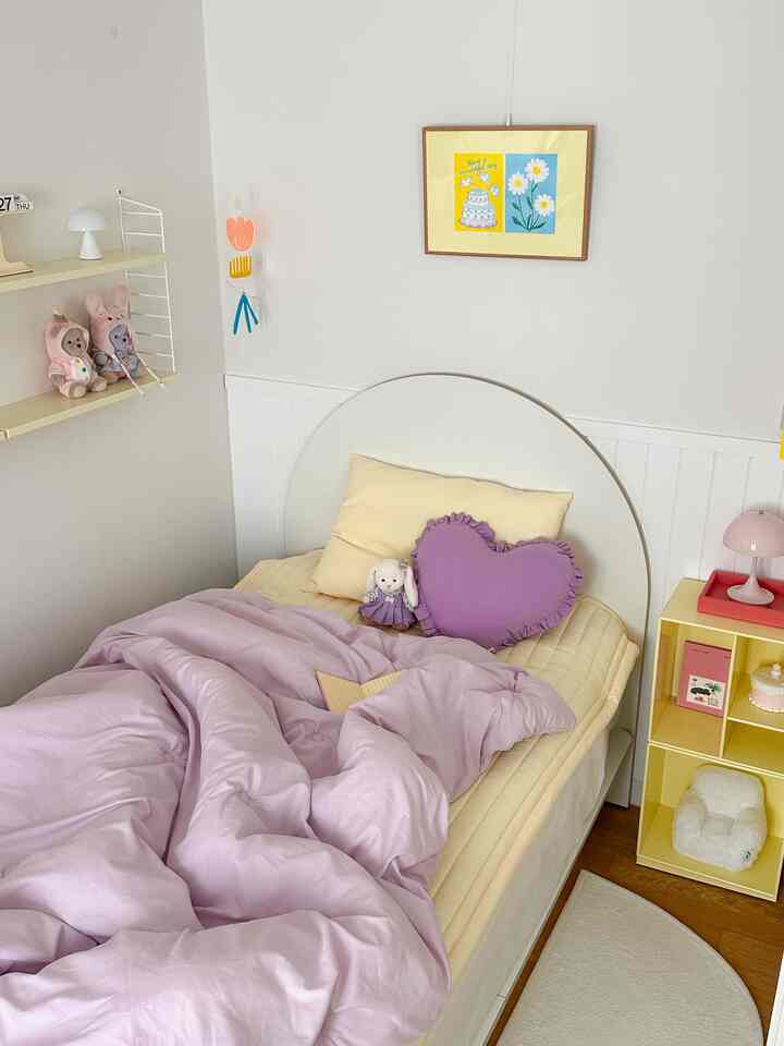 黄色とラベンダーの色調の子供部屋、アーチ型ヘッドボードのベッドと心地よい寝具が配置された温かみのあるインテリア