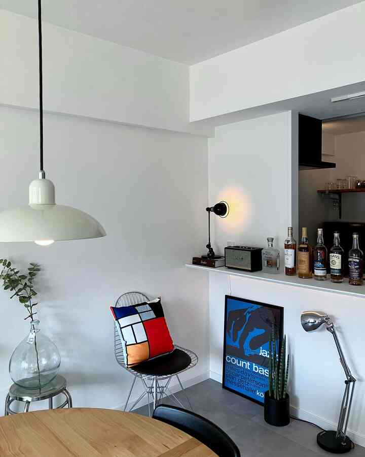 A white and black Mid-Century Modern home bar corner featuring a wire chair, colorful geometric cushion, and modern lighting fixtures