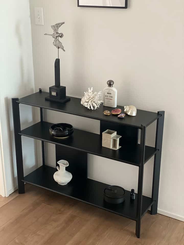 ナチュラルカラーの壁と木製床に黒い棚板が配置された玄関の雰囲気のあるディスプレイスペース