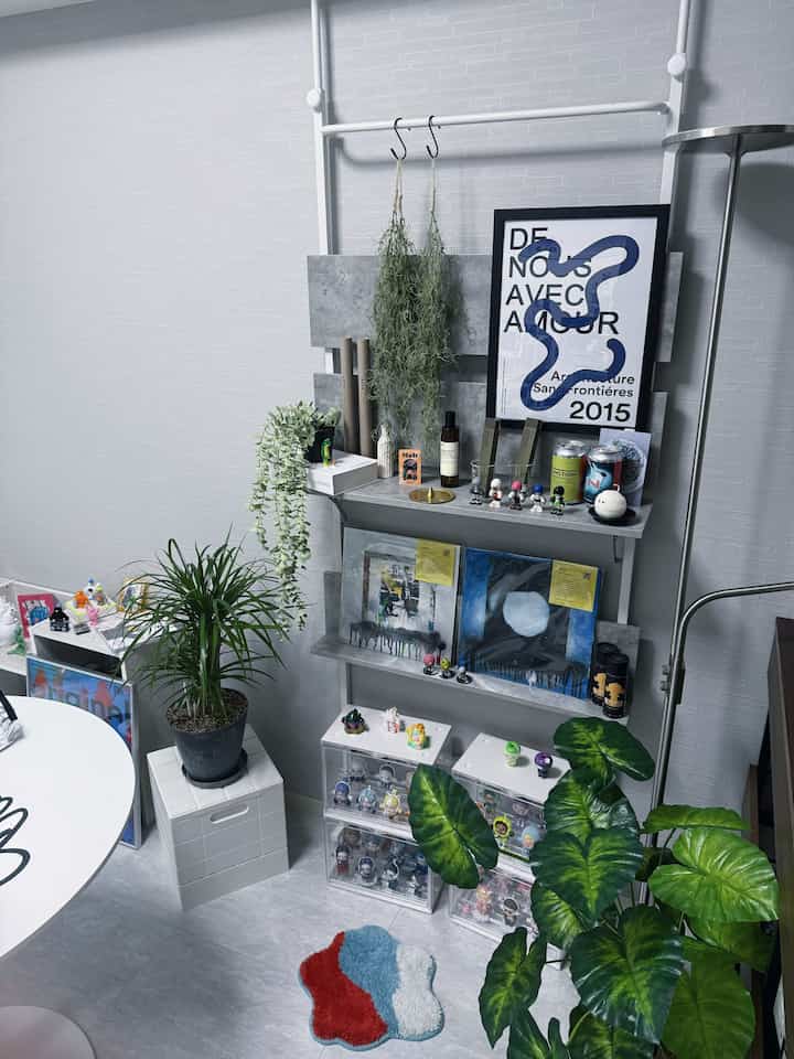 グレーとホワイトのトーンのリビングルーム、ディスプレイラックと多数の観葉植物、コレクションフィギュアが配置されたモダンで趣味的な空間