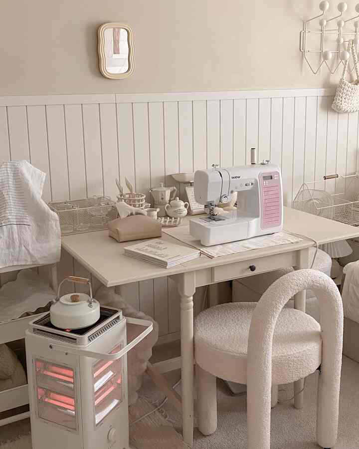 ベージュと白のトーンのワークスペース、ミシンとホーローケトル、ヒーターが配置された雰囲気のあるインテリア