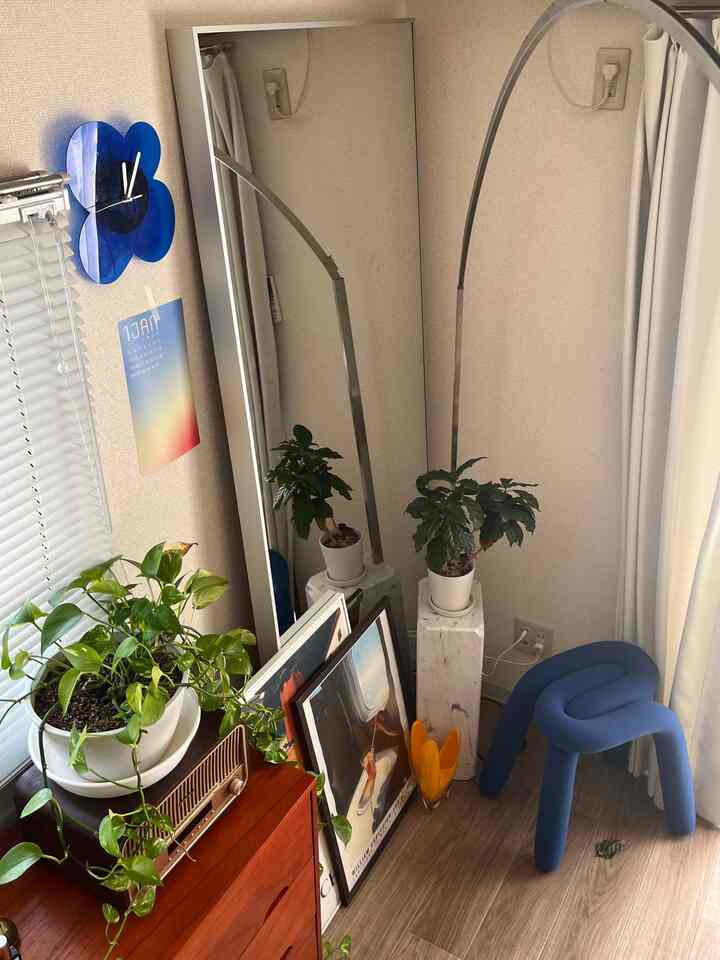 ナチュラルトーンの8畳リビング、大型の鏡と青いスツール、多様な植物が配置された印象的な空間