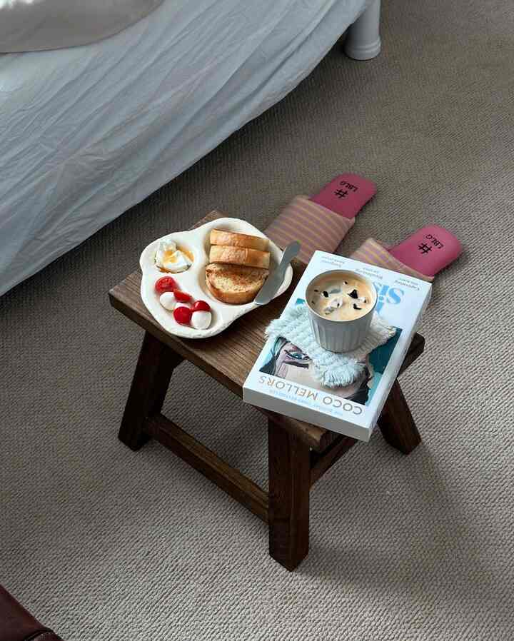 ナチュラルな色調の寝室、木製スツールに朝食とコーヒーが置かれた雰囲気のある空間