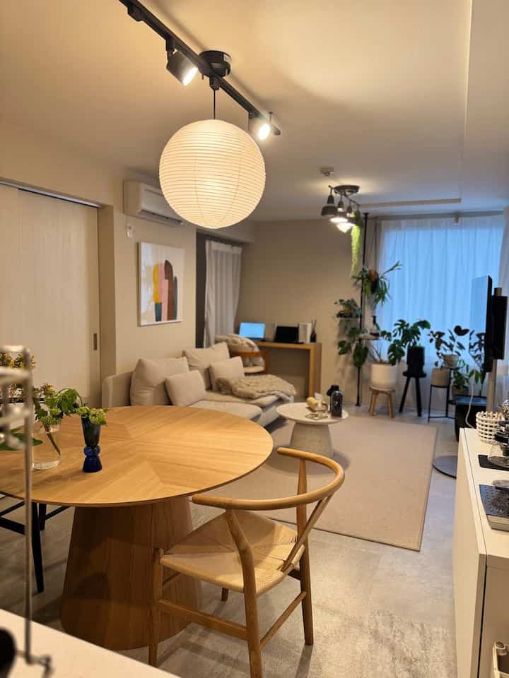 Natural tone 2LDK living and dining room featuring round wooden dining table, beige sofa, and pendant light with warm ambiance