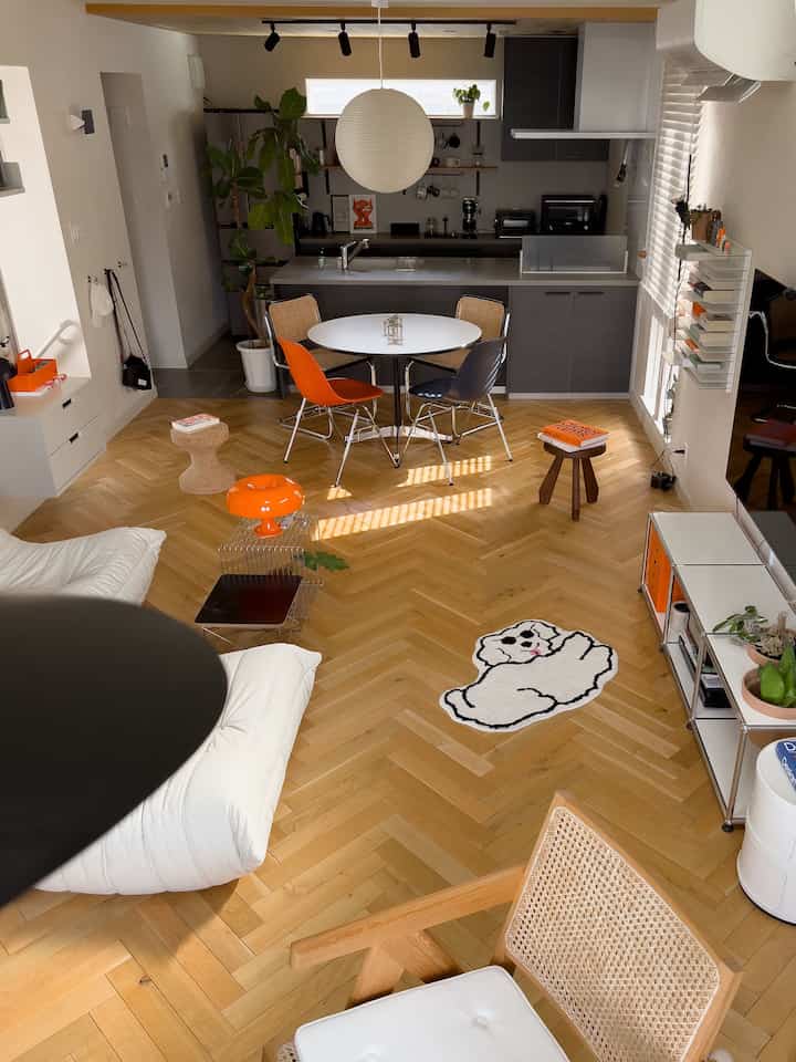 Modern living and kitchen space with mid-tone wood flooring and white table centerpiece, accented by vibrant orange elements