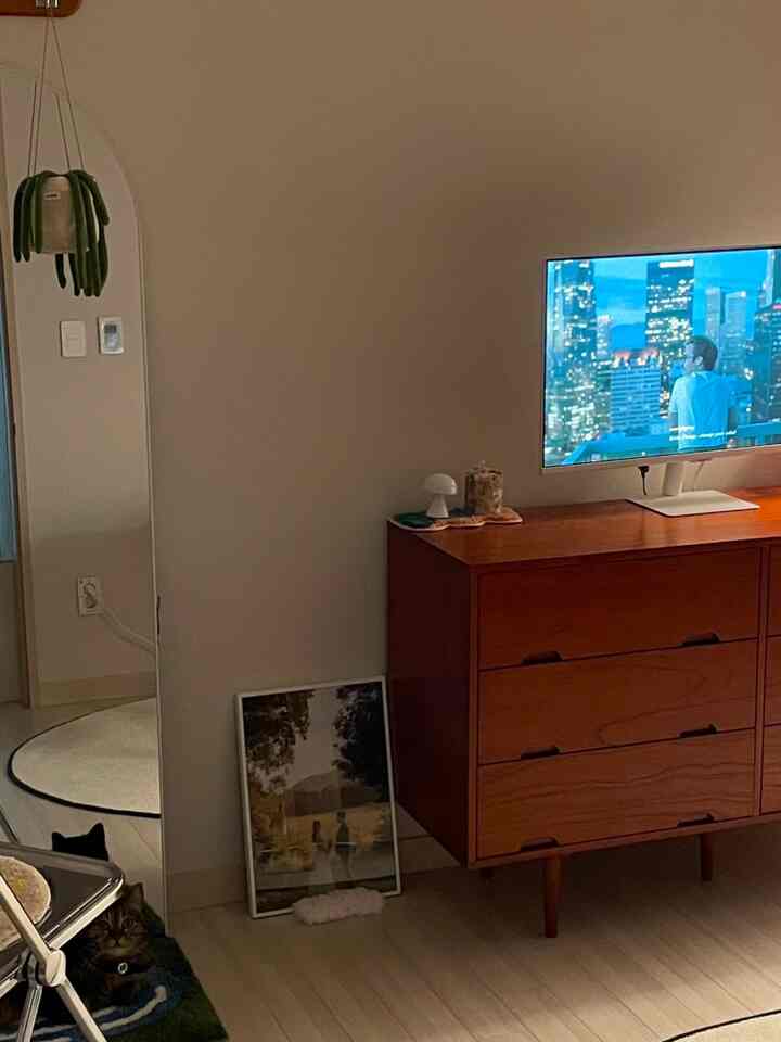 Beige walls and floor with a wood-toned dresser holding a TV monitor in a minimalistic space, cat resting on lower left corner