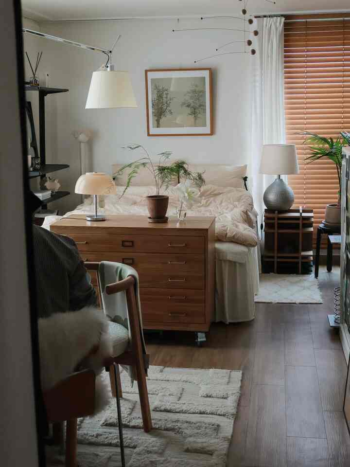 白と茶色のトーンが特徴のワンルーム寝室。木目調家具とラグ、照明が配置された雰囲気のあるインテリア