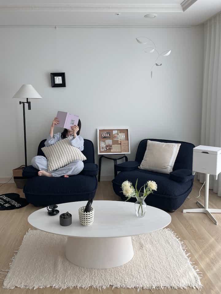 白い壁とナチュラルな木目調の床が印象的なリビング、ネイビーカラーのアームチェア2脚と白い楕円形のコーヒーテーブルが配置されたシンプルモダンで落ち着いたインテリア