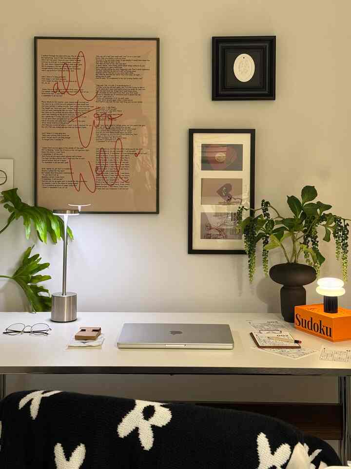 白い壁とすっきりとしたデスクがあるミニマルなホームオフィス空間、額装アートと植物が調和した洗練された作業環境