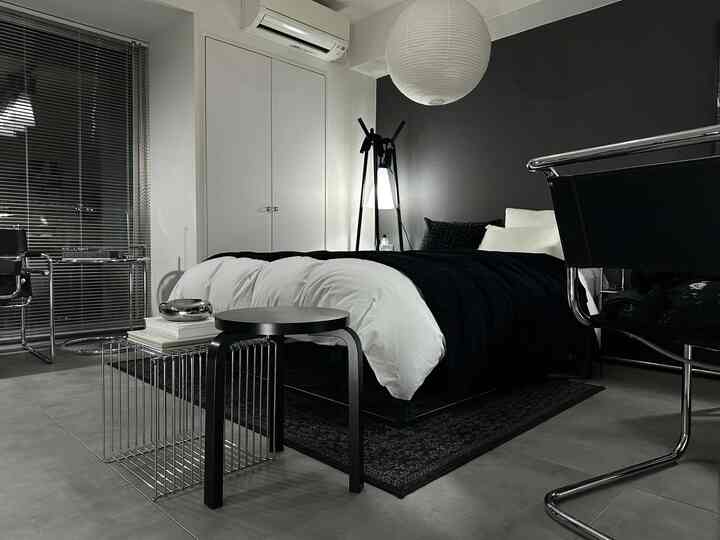 Modern bedroom with black and white tones featuring a large central bed, metal armchairs on each side, and a minimalist design