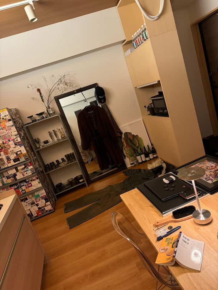 白い壁とブラウンの木目調が特徴の1LDKの空間、全身鏡と棚が配置された整頓されたインテリア