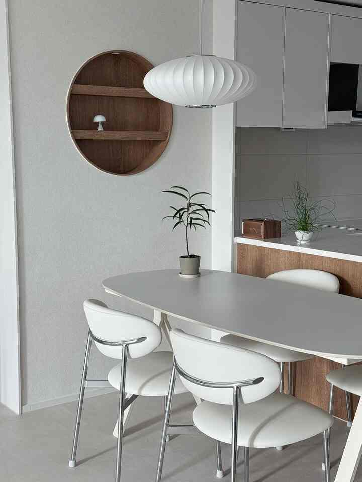 ホワイトと木目調が調和したキッチン空間、ミニマルなダイニングテーブルと椅子、ペンダントライトが配置された清潔感のあるインテリア