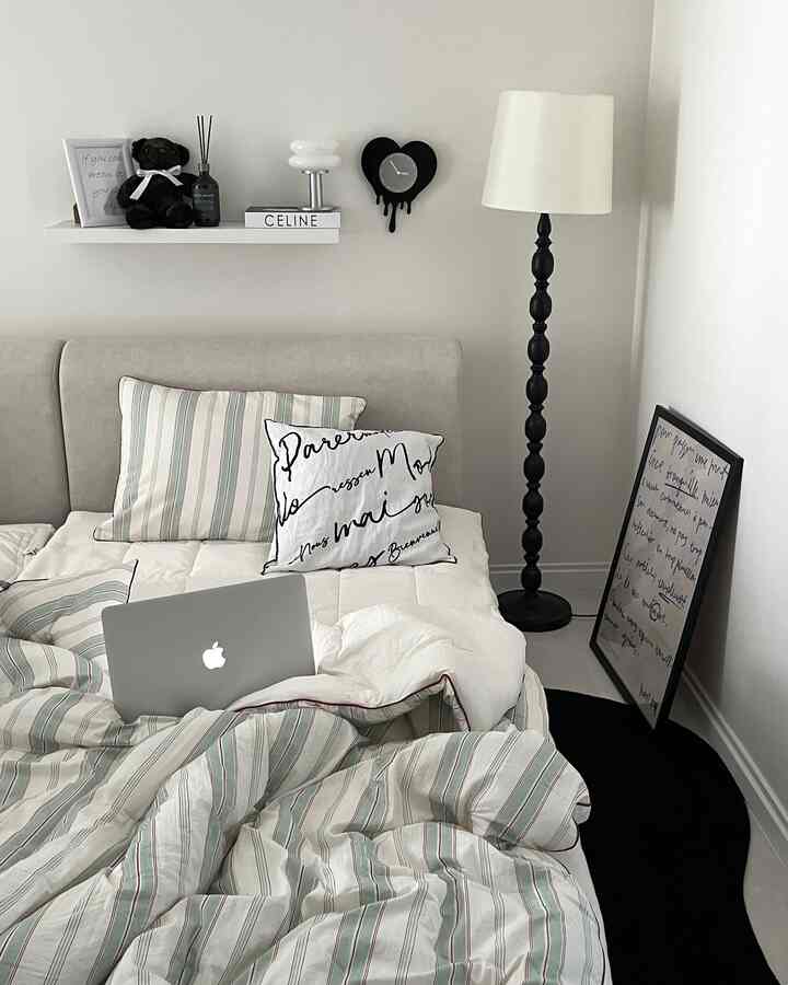 ホワイトとブラックのモノトーン寝室、ストライプの寝具とブラックのフロアランプが配置された印象的な空間