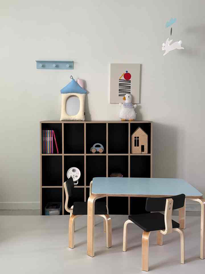 白を基調としたリビングの子供部屋、パステルブルーのテーブルと木製の本棚が清潔感と自然な雰囲気を演出している