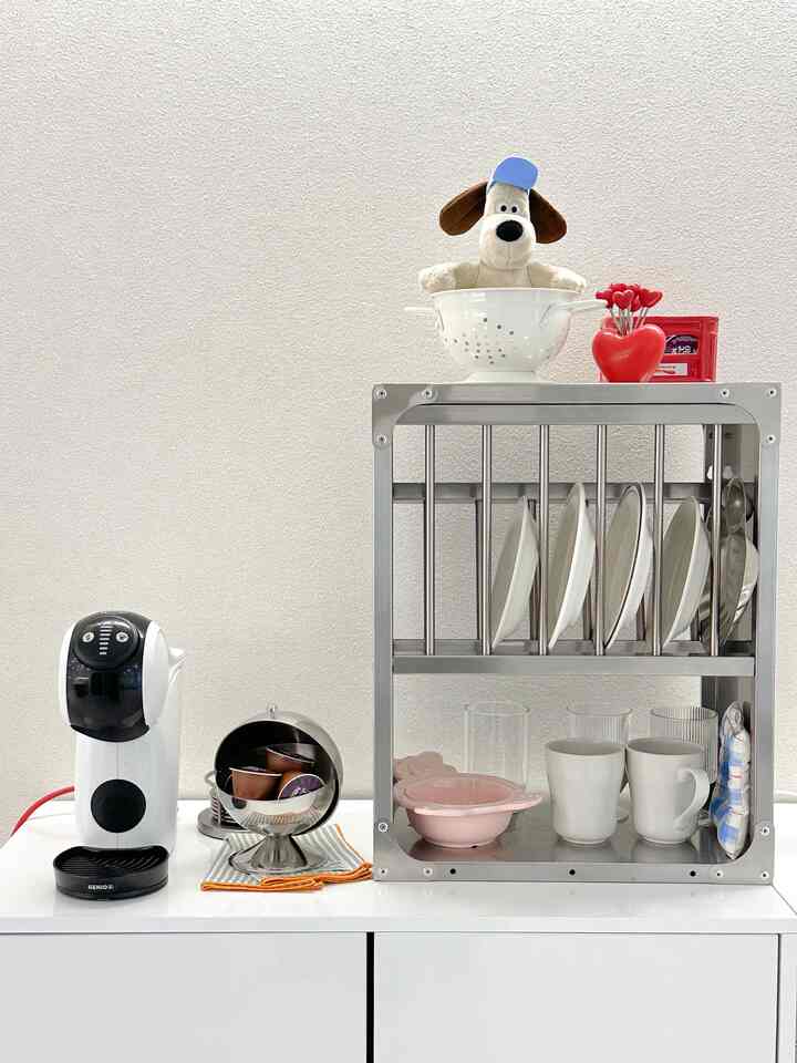 White-toned kitchen storage space featuring a capsule coffee machine and kitchen rack with neatly arranged plates and mugs in a minimal home cafe corner