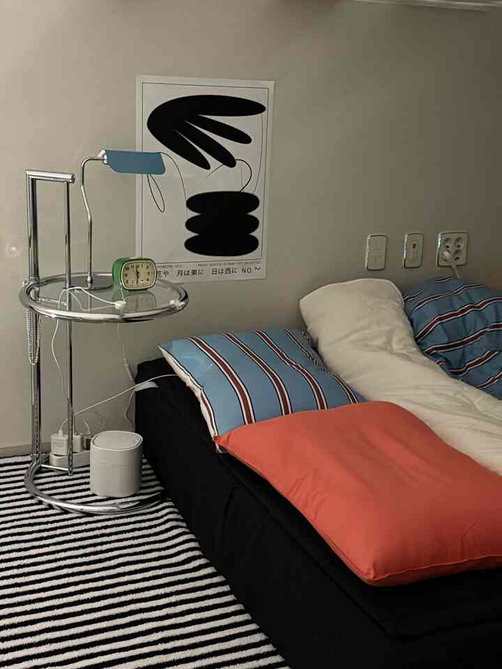 ブラックのソファと青いストライプの枕があるミッドセンチュリーモダンの寝室、メタルのナイトテーブルとテーブルランプが配置された雰囲気のあるインテリア