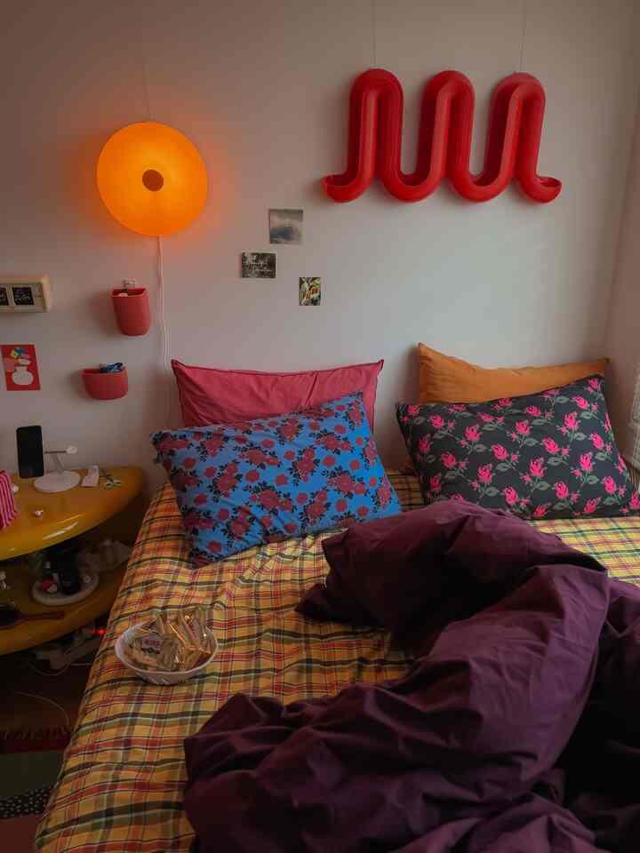 黄色と赤色のトーンが調和した寝室、様々なパターンの枕と掛け布団カバーが配置された雰囲気のあるインテリア