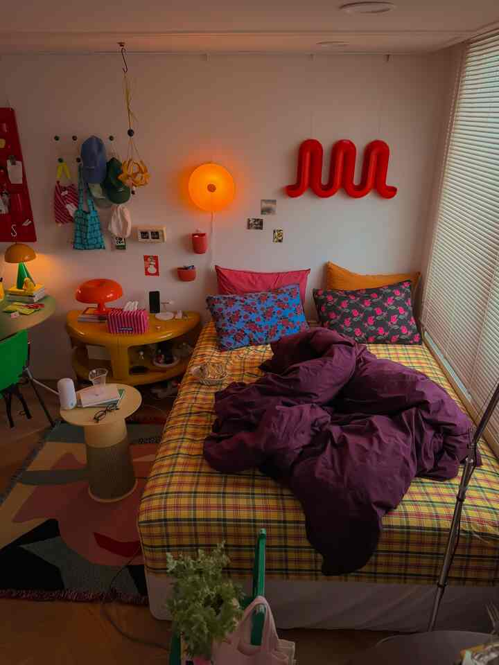 黄色と紫の寝具が置かれたワンルームの寝室、多彩な壁の装飾と照明が調和した雰囲気のあるインテリア