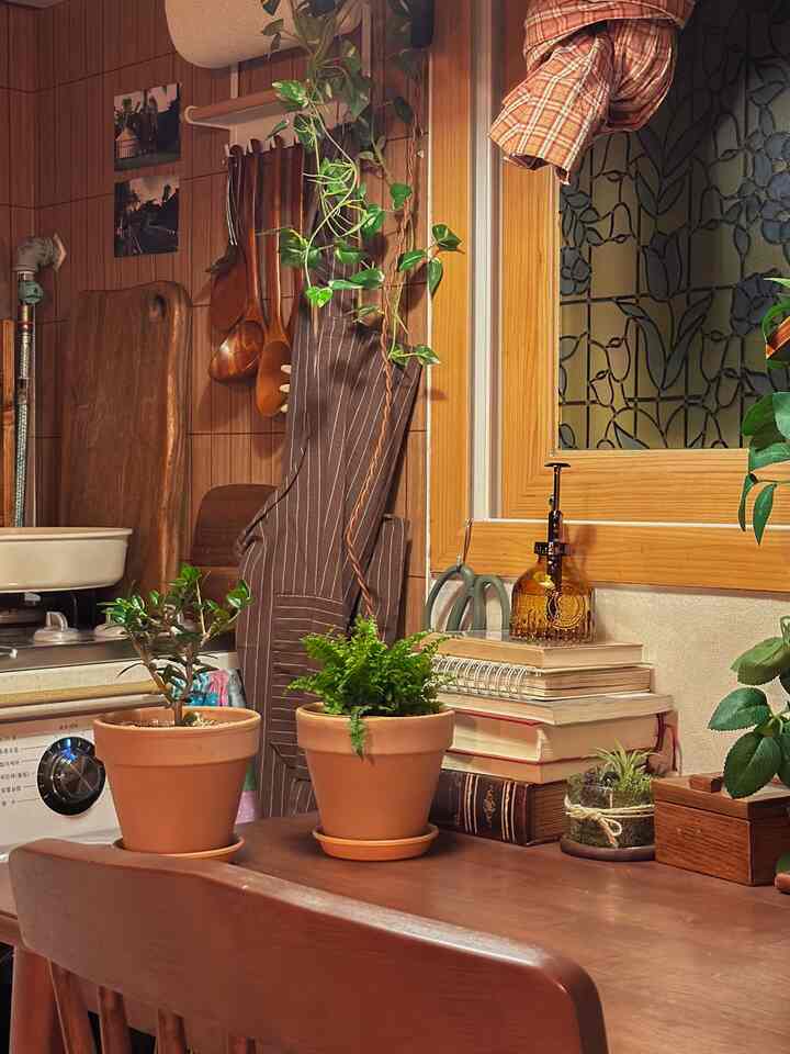 暖かいナチュラルカラーのキッチン、木製のテーブルに多様な植物とキッチン用品が配置された雰囲気のある空間