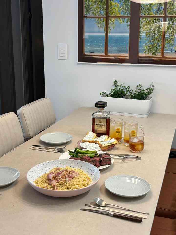 ベージュの色調のキッチンスペース、中央にダイニングテーブルと白い椅子が配置され、ホームパーティーの料理とドリンクが並ぶ雰囲気のあるインテリア