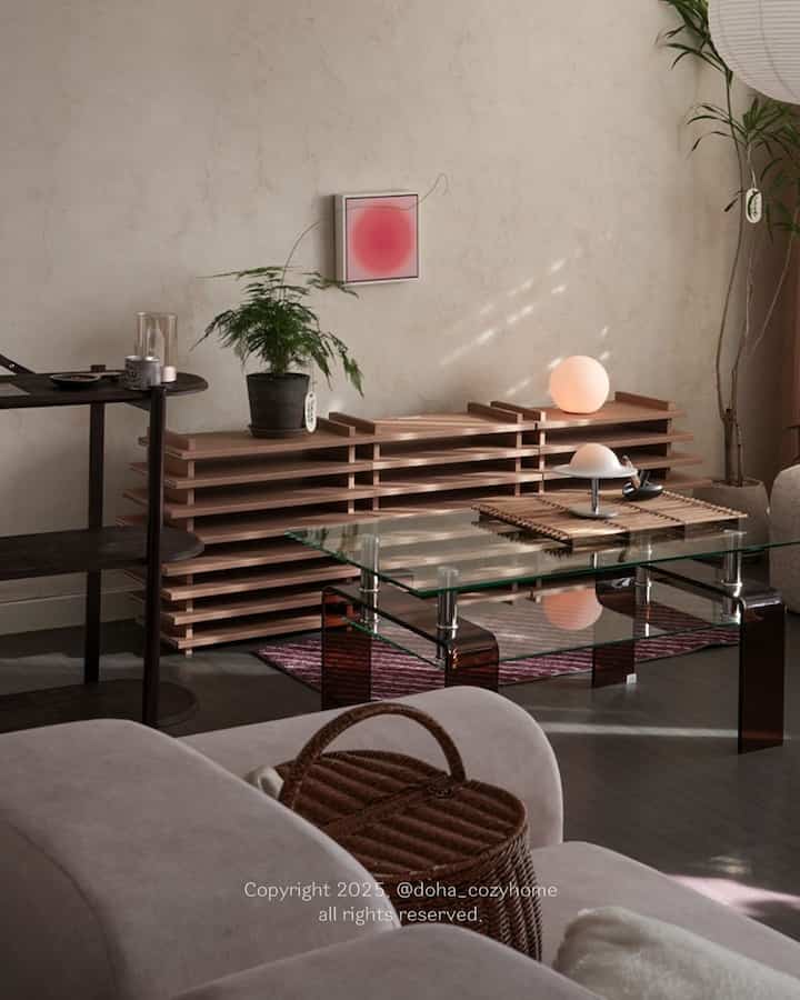 A living room with wood tones and golden hour lighting, featuring a glass coffee table and various plants in a calm atmosphere