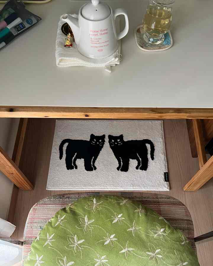 ホワイトテーブルとグリーンクッション、黒猫柄のラグが配置された温かみのあるダイニングスペース