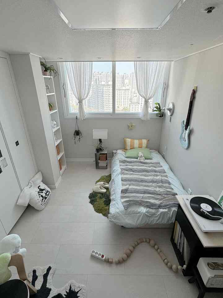 白と緑の色調の狭い寝室、シングルベッドと本棚、サイドテーブルが配置された雰囲気のある空間