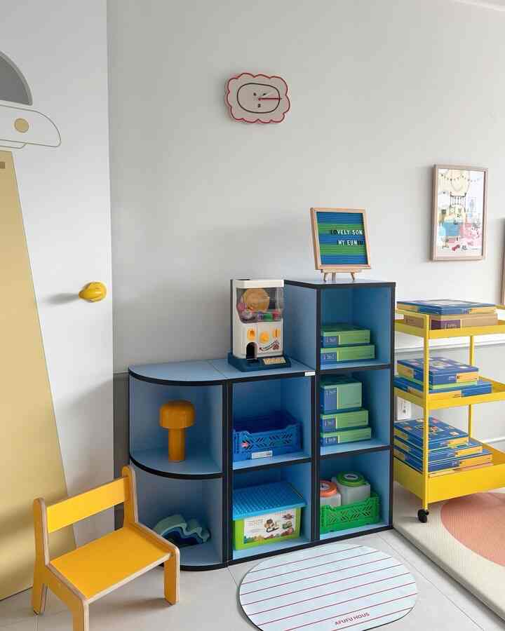 明るい白い壁とパステルブルーの収納がある子供部屋、黄色の子供用椅子とおもちゃが配置された雰囲気のあるインテリア