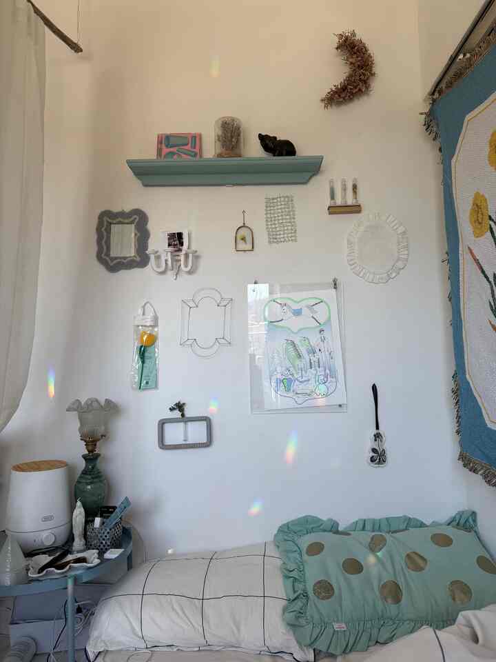 Natural-toned bedroom in whites and soft greens featuring a bed, nightstand, and various decorative wall items creating a cozy atmosphere
