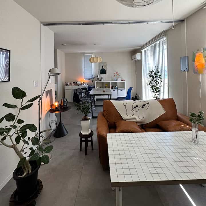 Modern single household living room with white walls and brown leather sofa, featuring a dining table, floor lamp, and plants creating a cozy atmosphere