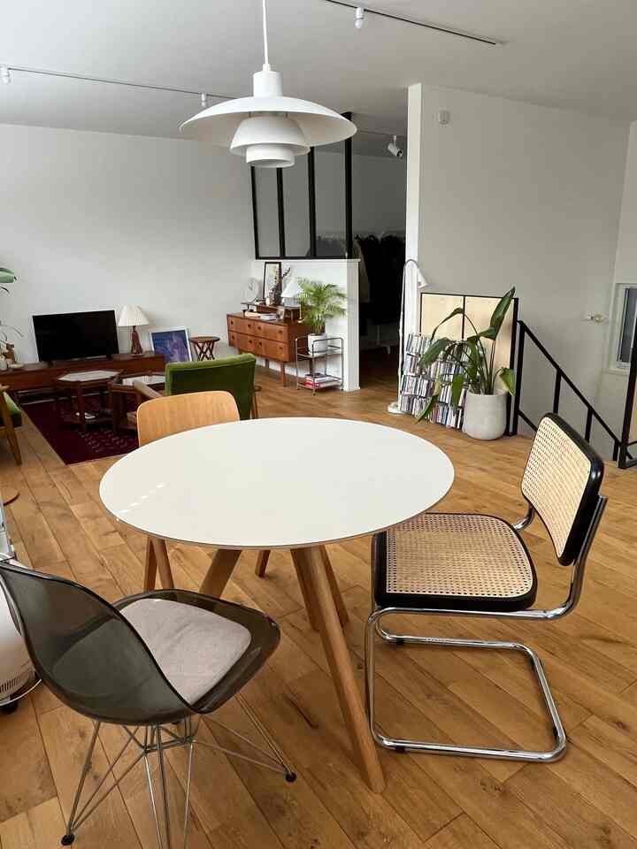 Natural-toned living and dining room with white walls and wood flooring, featuring modern furniture and pendant lighting