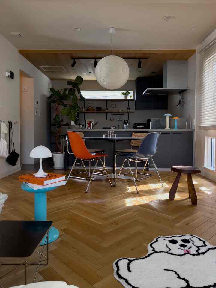 モダンな印象のダイニングルーム、オレンジ色のチェアとスカイブルーのスツールが配置された木目調の温かみある空間