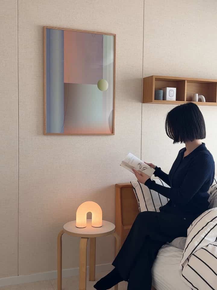 ベージュの壁と白い寝具、木製スツールにアーチ型のテーブルランプが配置された、自然で落ち着いた雰囲気の寝室