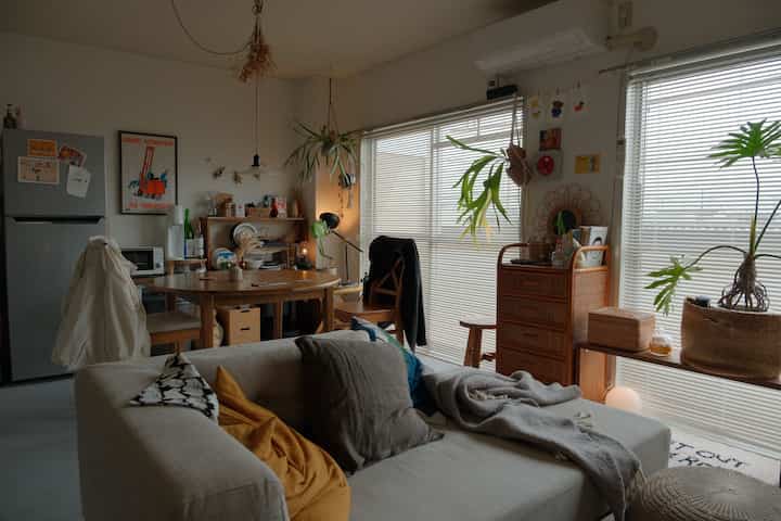 Natural-toned 12-tatami living dining room featuring beige sofa, wood dining table, plants by window blinds creating cozy interior