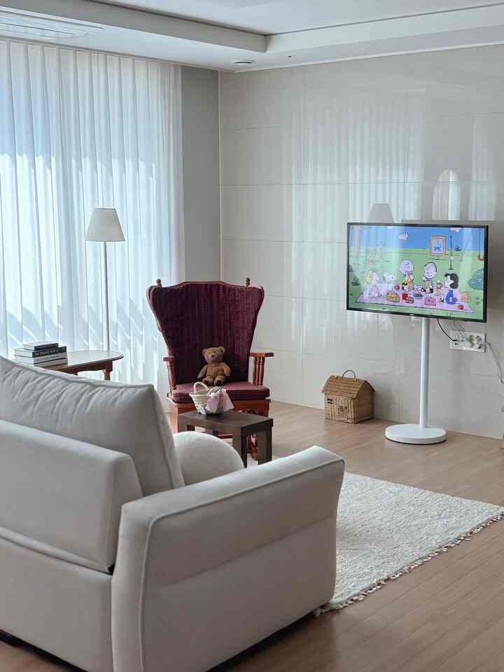 A modern and natural living room in white and brown tones featuring a white sofa, wooden floor, burgundy armchair, and white TV stand