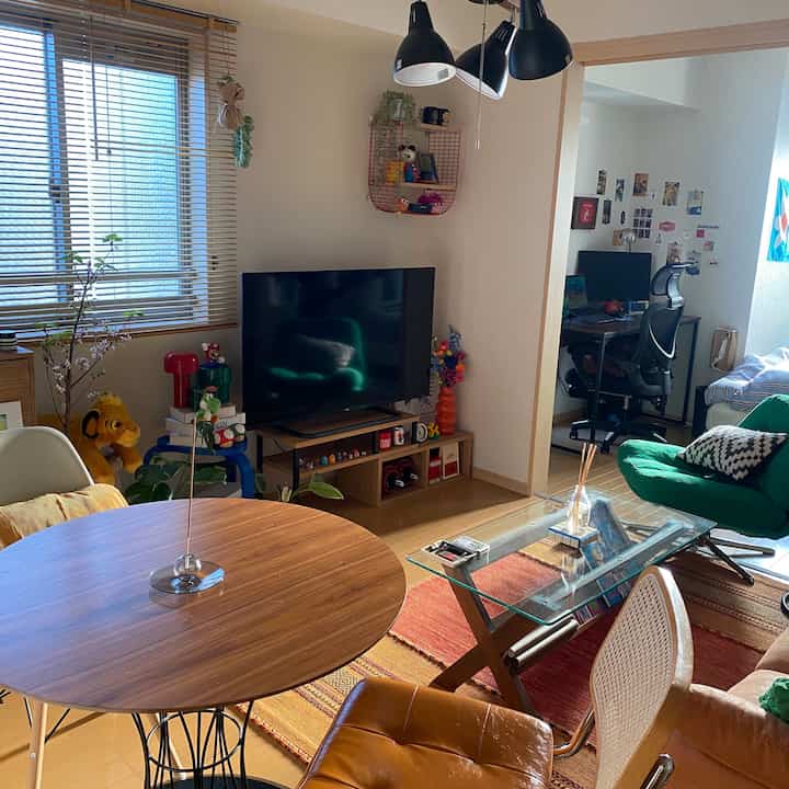 自然な木目調が特徴の二人暮らし用リビングルームとホームオフィススペース、緑色のアームチェアと白いソファが配置された居心地の良いインテリア