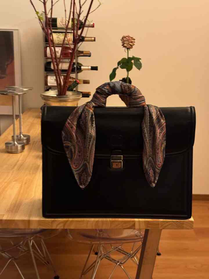 ナチュラルな色調のダイニングルームで、木製テーブル中央に黒いバッグが置かれた落ち着いた空間