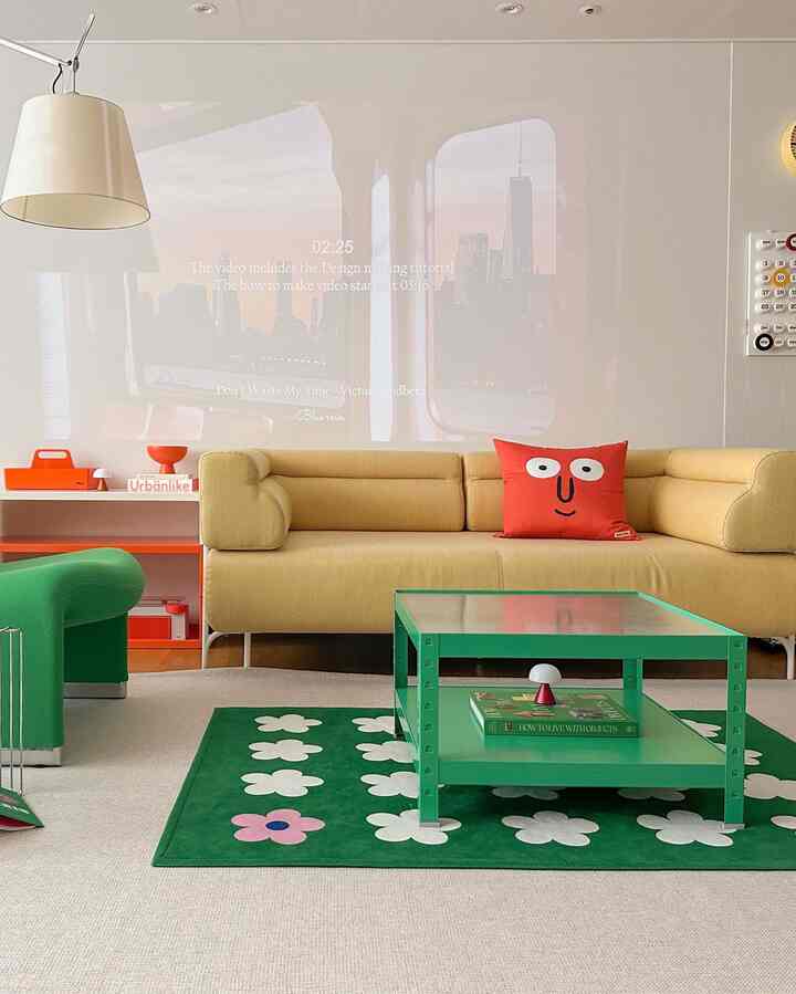 Bright, modern living room featuring a yellow sofa with a red face cushion, green floral rug, and green coffee table
