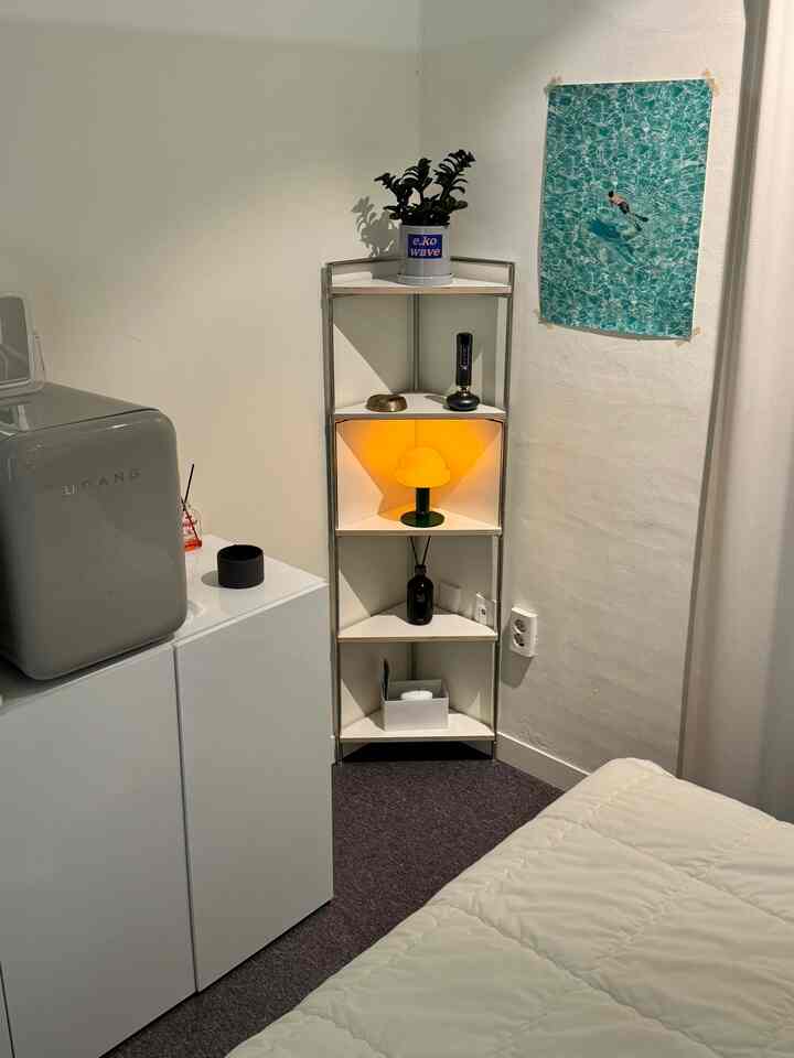 白を基調とした狭い部屋のコーナーに配置された棚と小物があるミニマルでナチュラルな印象の管理室空間