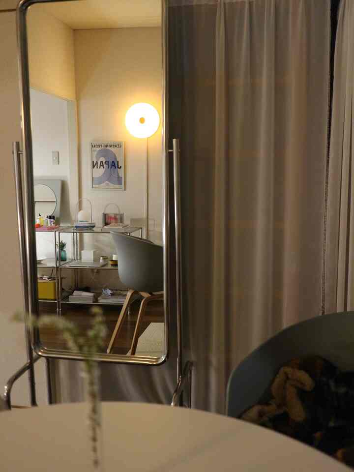 Silver-framed full-length mirror centered, reflecting a Mid-Century Modern living room interior with lamp, chair, and shelving unit