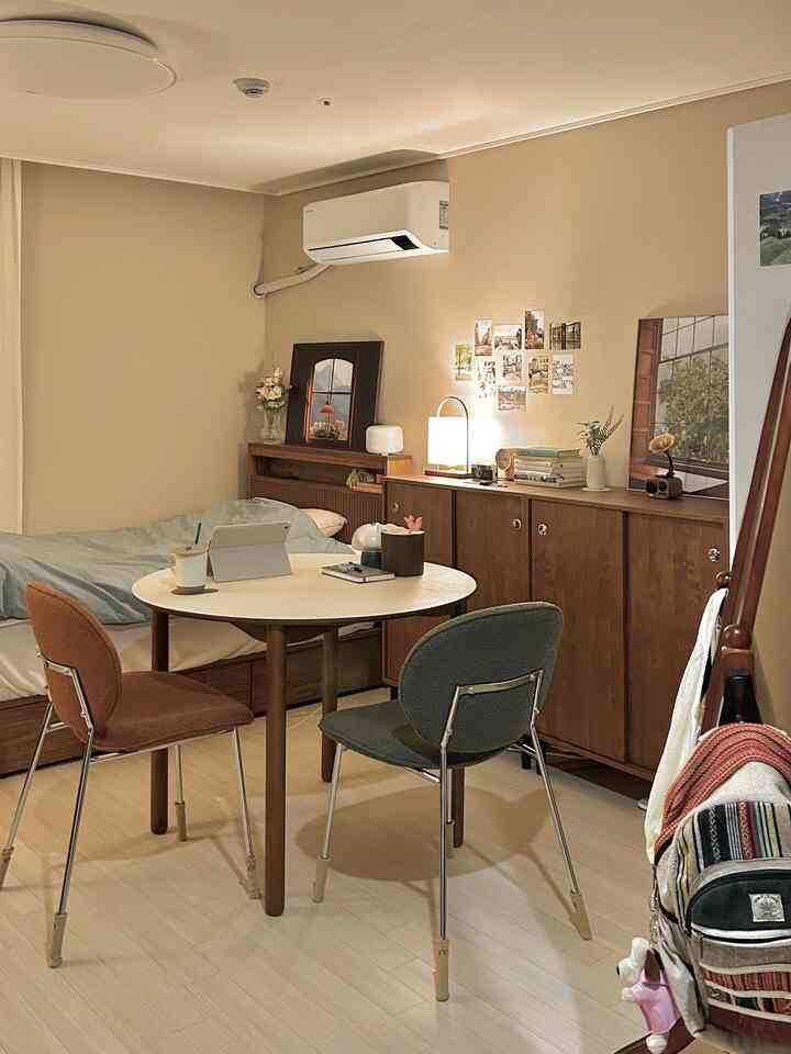 暖かみのある木目調とベージュの壁のワンルーム、ベッドと丸テーブル、ブークレチェアが配置された落ち着いた空間