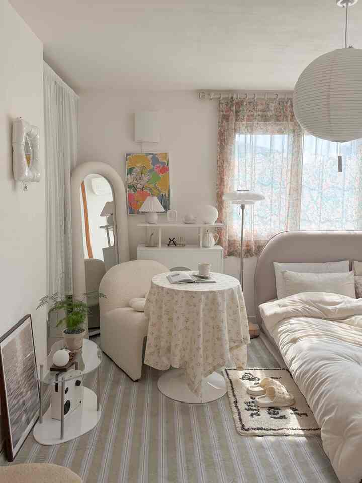 白とアイボリーの色調の寝室、アームチェアと丸いコーヒーテーブル、フロアランプが配置された雰囲気のある空間