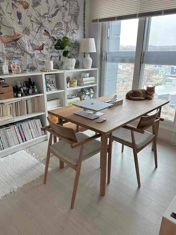 ナチュラルトーンのダイニングルーム、木製のダイニングテーブルと椅子2脚が配置された暖かみのあるホームオフィス空間、テーブルの上に猫が座っている