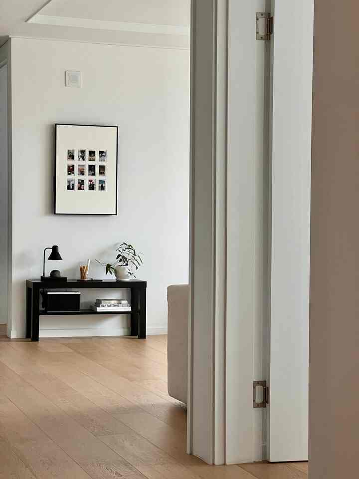 白い壁と木目調の床のリビング、シンプルでモダンな空間に黒いテーブルランプと額縁が配された印象的なインテリア