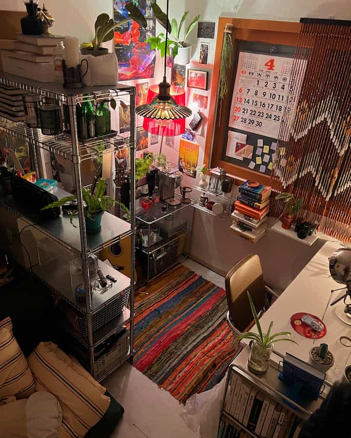 温かみのあるレトロ調の1.5坪の小部屋、金属製の棚とカラフルなラグ、デスクや多様な小物が配置された居心地の良い空間