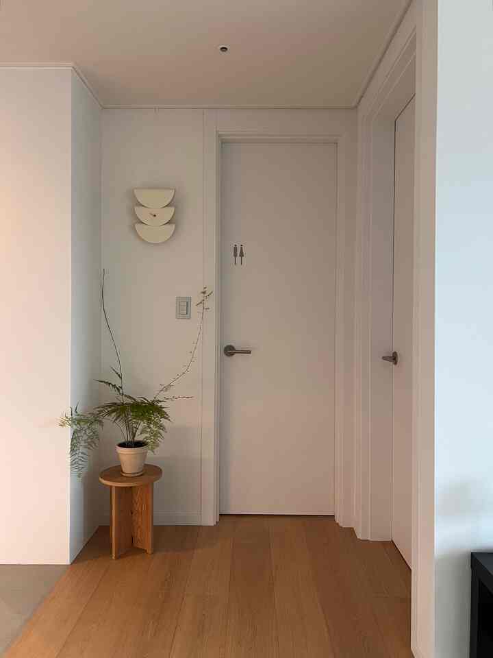 白と茶色のトーンの玄関ホール、小さな木製サイドテーブルと観葉植物が配置された清潔でミニマルな空間